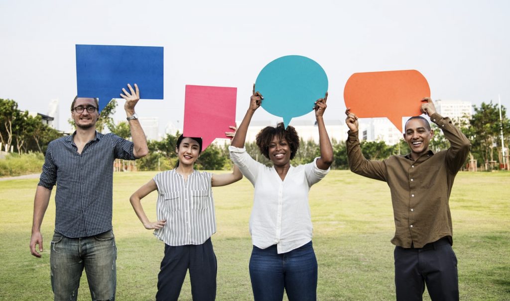 Two man and two woman standing on green grass holding cardboard speech balloon above their head